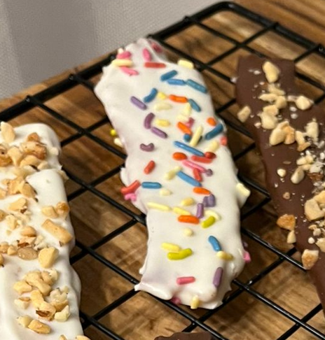 Banana dipped in white chocolate and rainbow sprinkles on a cooling rack.