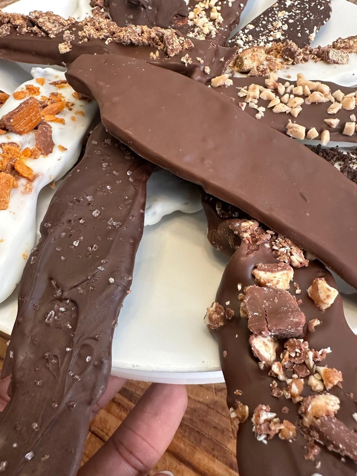 Close-up of a plate holding chocolate-covered toffee bark, some topped with nuts.
