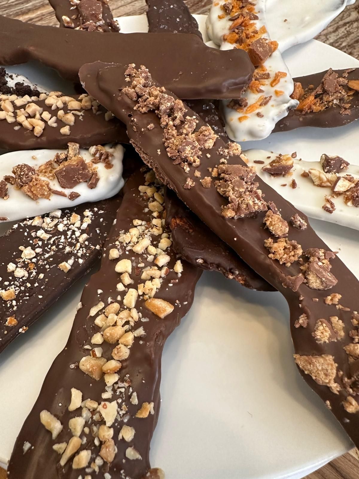 Chocolate-covered toffee, milk and white chocolate, with chopped nuts and candy pieces on a white plate.