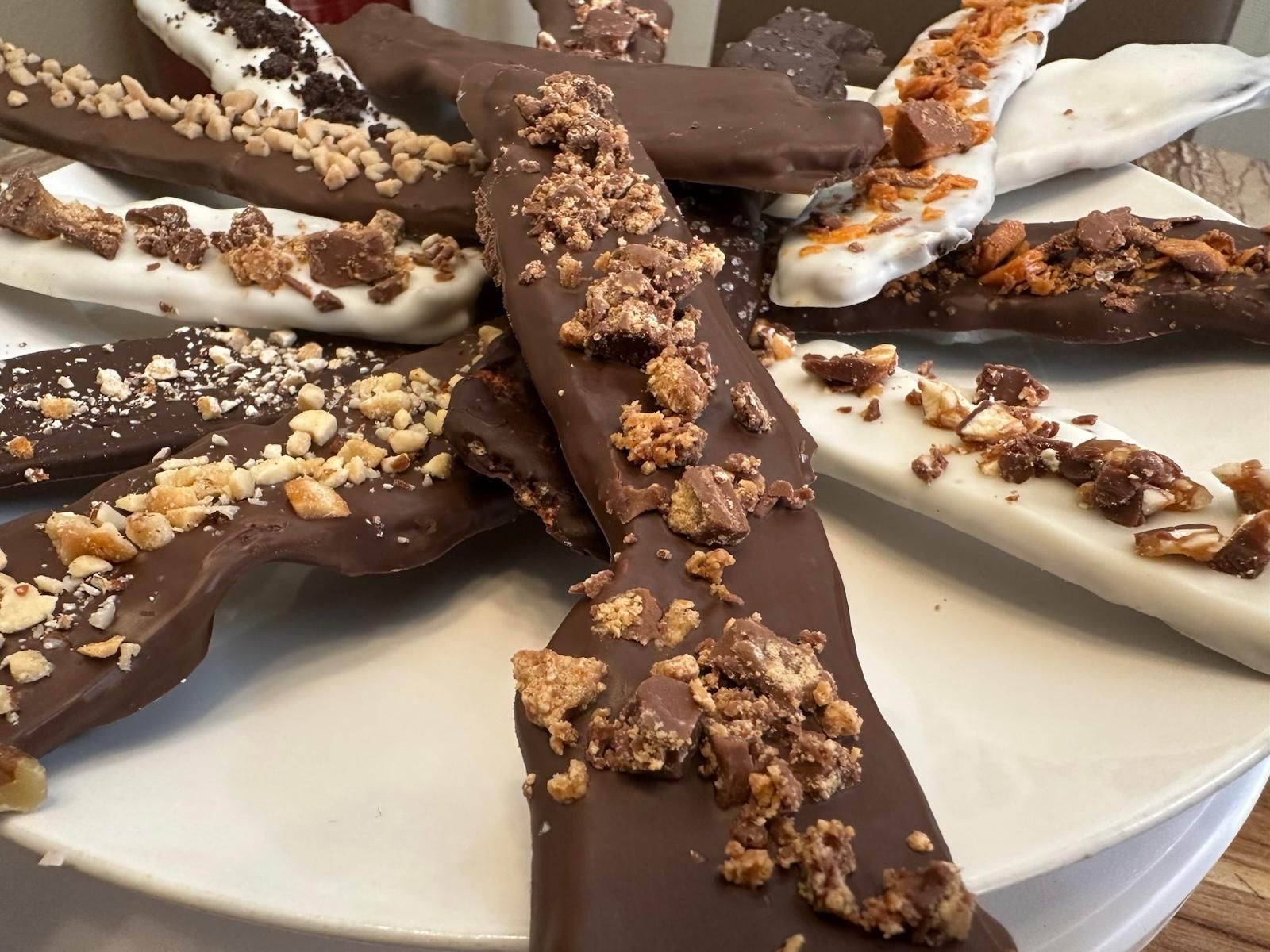 Chocolate bark on a white plate, topped with nuts and candy pieces.