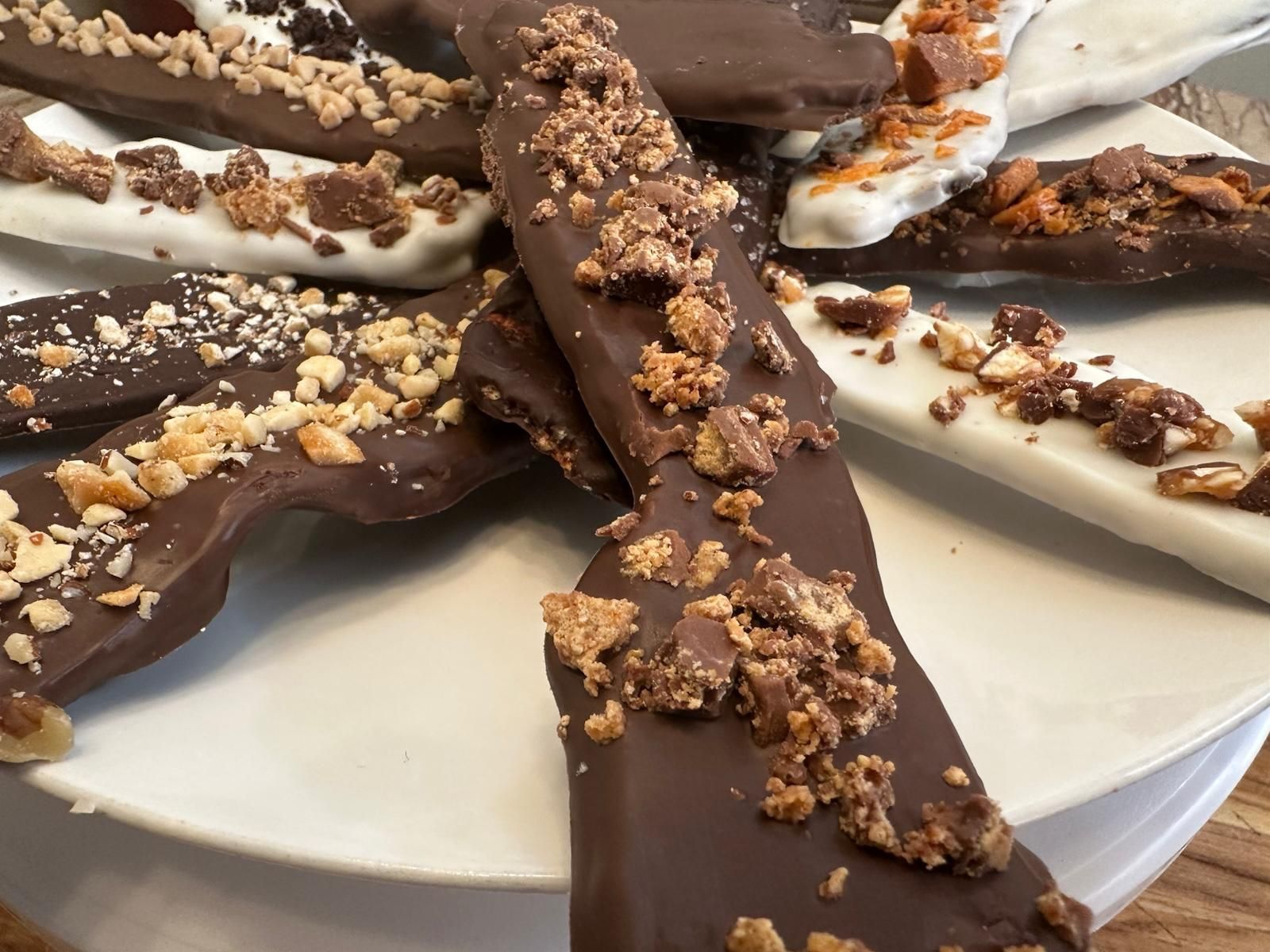 Chocolate-covered banana slices on a white plate, decorated with crushed nuts and toffee bits.