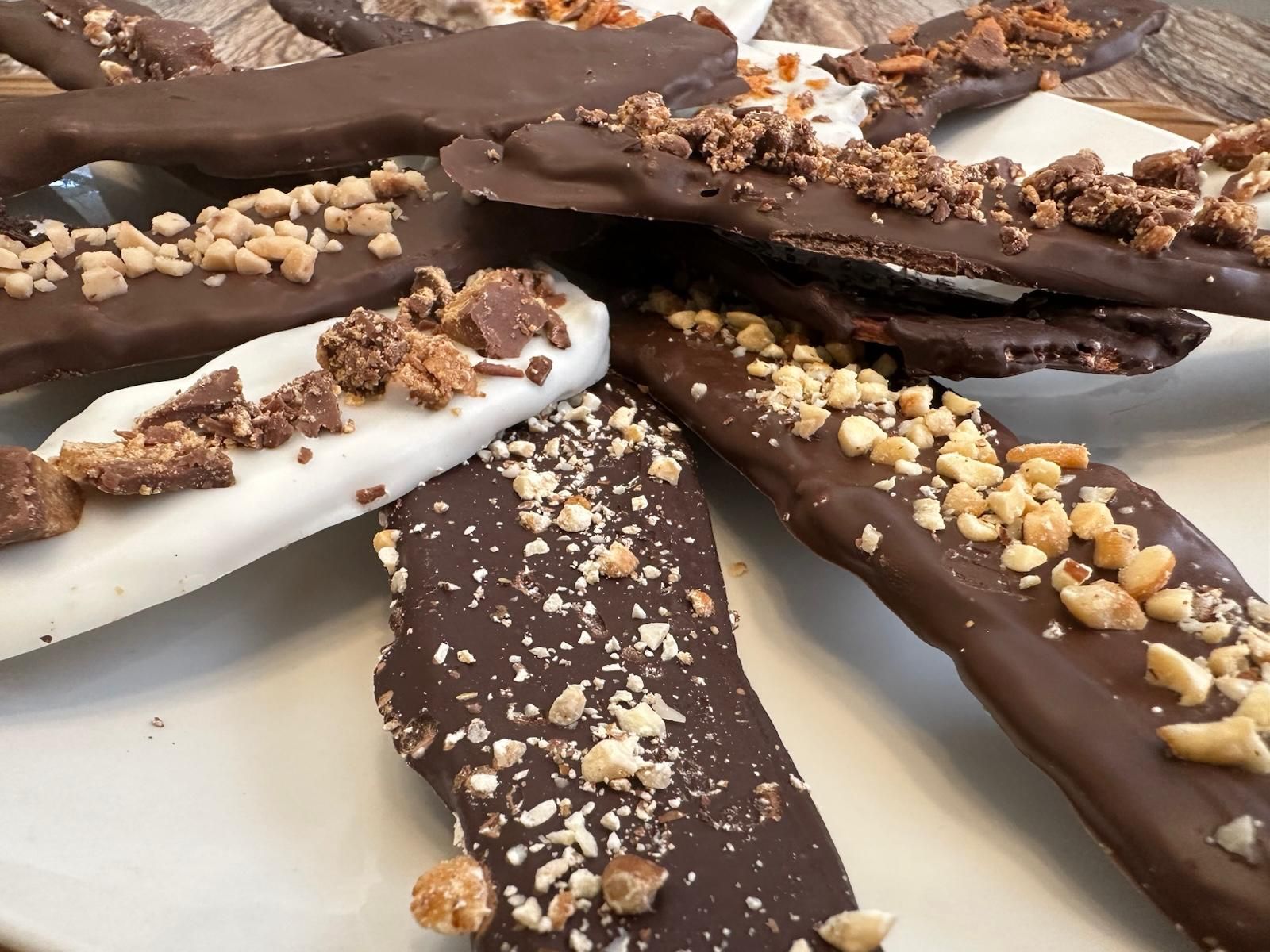 Chocolate-covered banana slices with various toppings like nuts and candy pieces on a white plate.