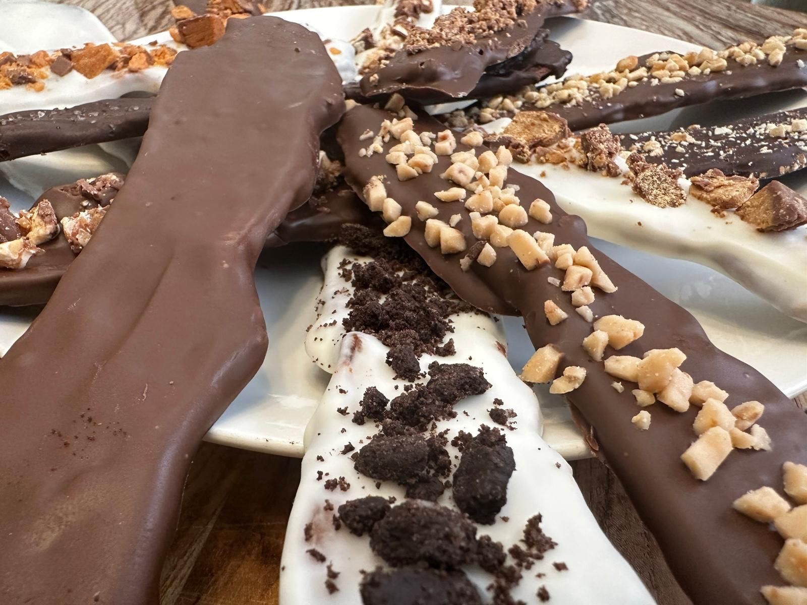 Chocolate-covered pretzel rods with various toppings (toffee, cookie crumbs) on a white plate.