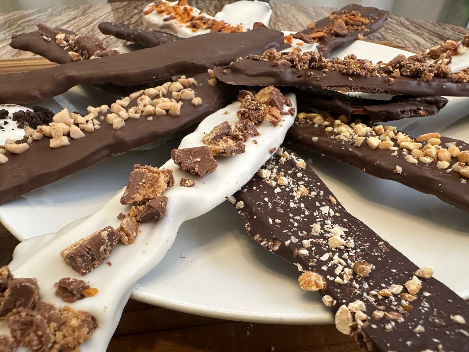 Chocolate-covered pretzel sticks with various toppings on a white plate.