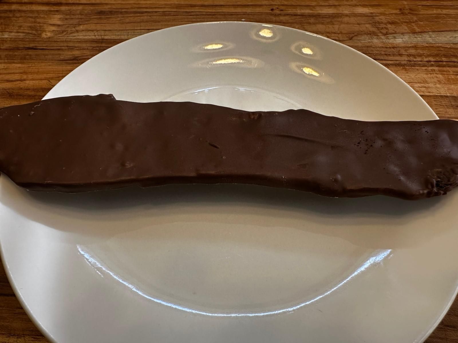 Dark chocolate-covered candy bar on a white plate, set on a wooden surface.