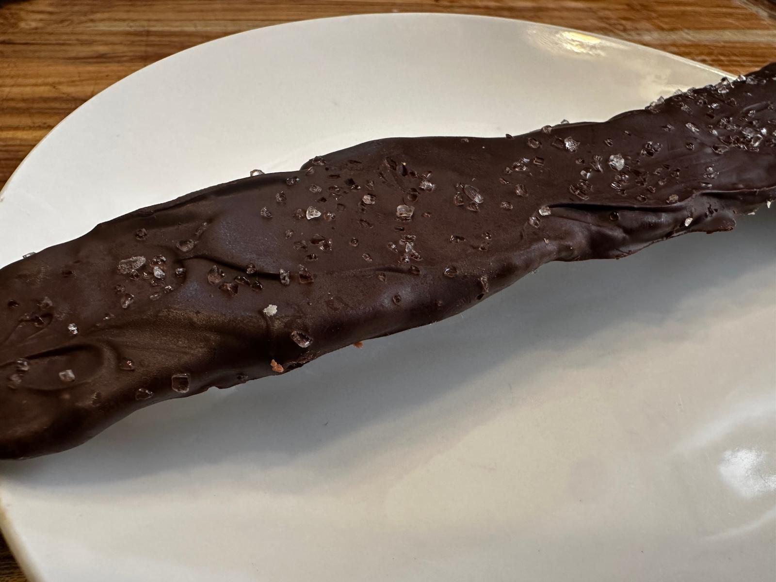 Dark chocolate-covered pretzel stick on a white plate, sprinkled with sea salt.