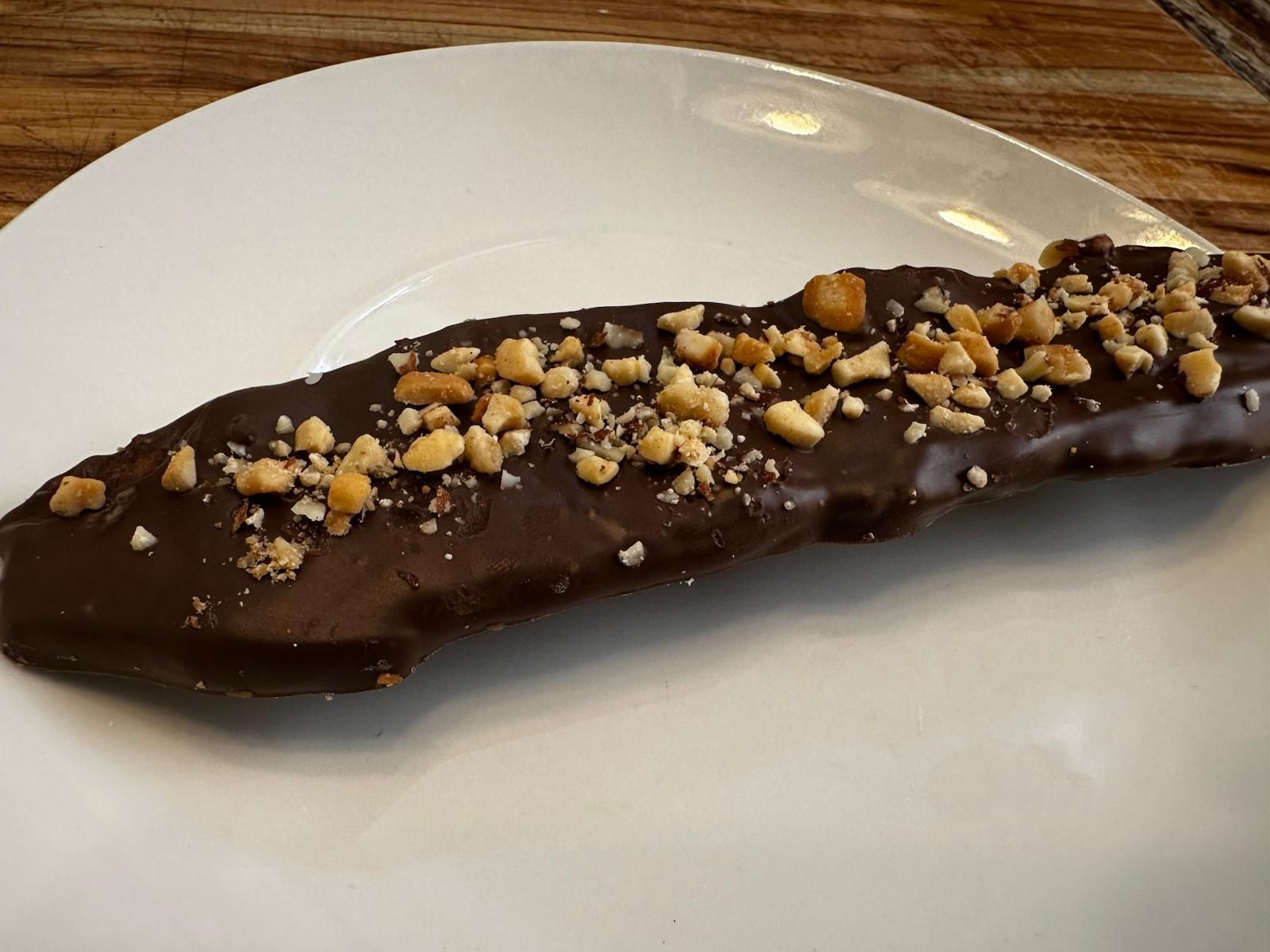 Chocolate-covered banana topped with chopped nuts on a white plate.