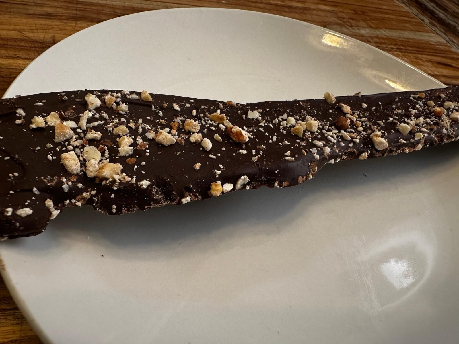 Chocolate-covered toffee bar with chopped nuts on a white plate.
