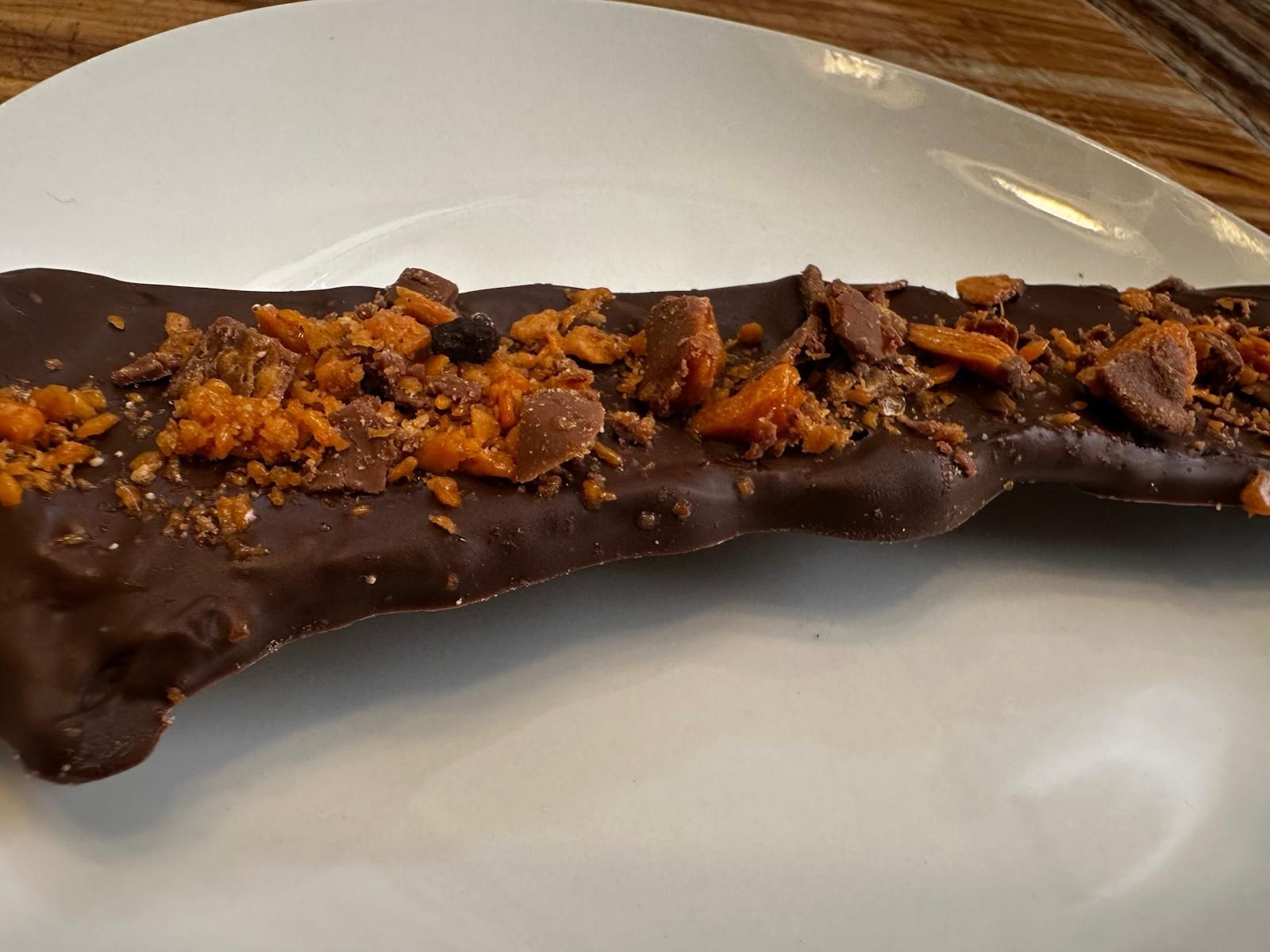 Chocolate-covered toffee bar on a white plate, topped with crushed toffee pieces.