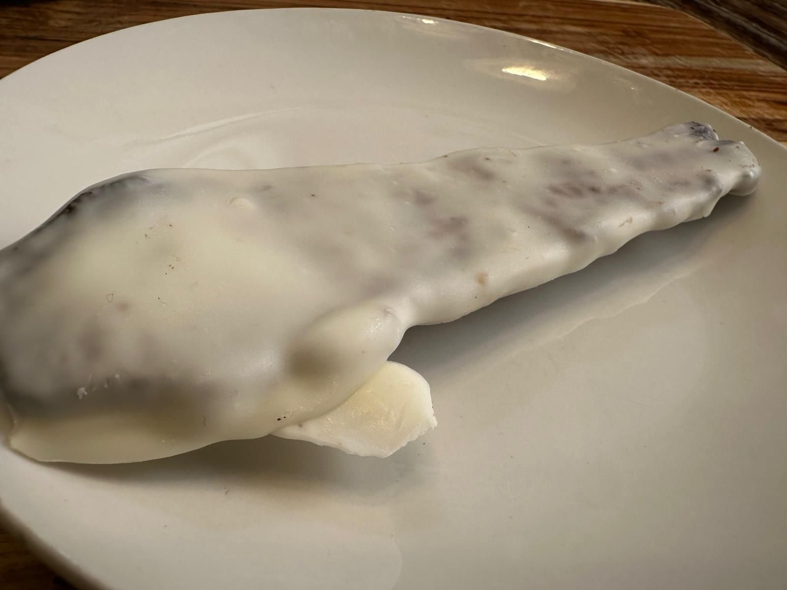 A fish fillet covered in white sauce on a white plate.