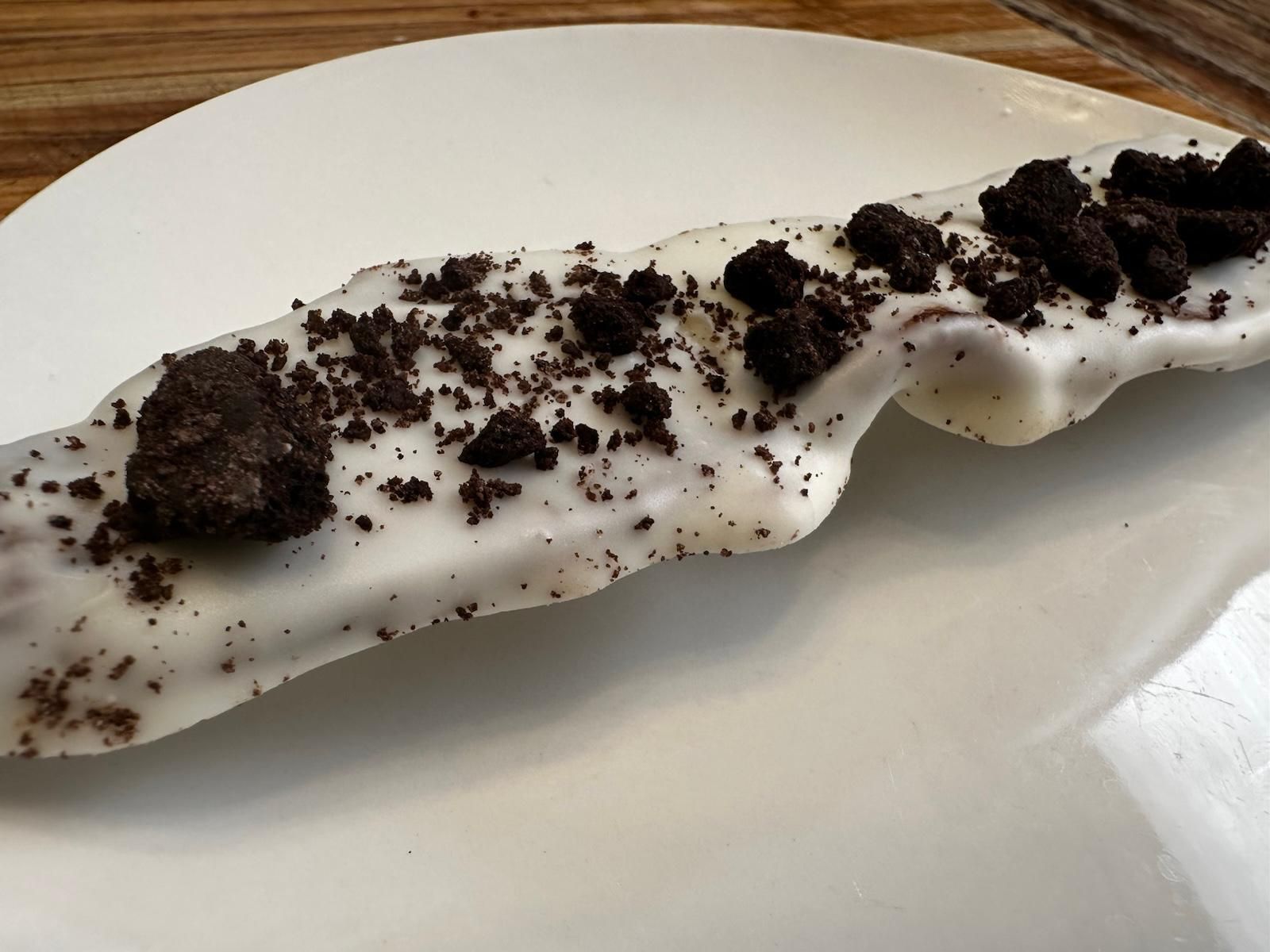 White-frosted pastry topped with crushed Oreo cookies on a white plate.