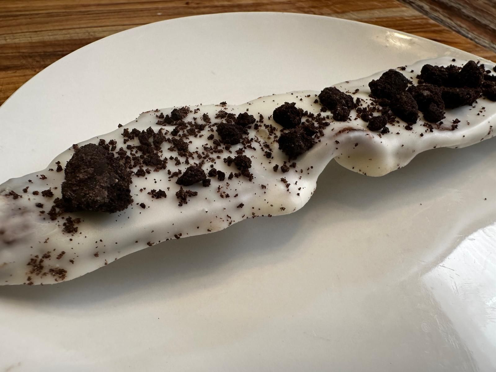 White-chocolate-covered pretzel sprinkled with crushed Oreo cookies on a white plate.