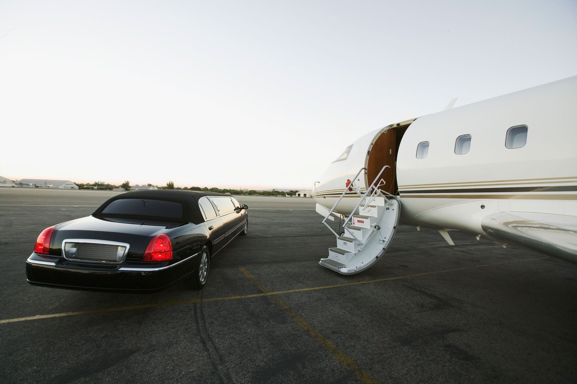 Luxurious stretch limo parked beside a private jet at the airport.