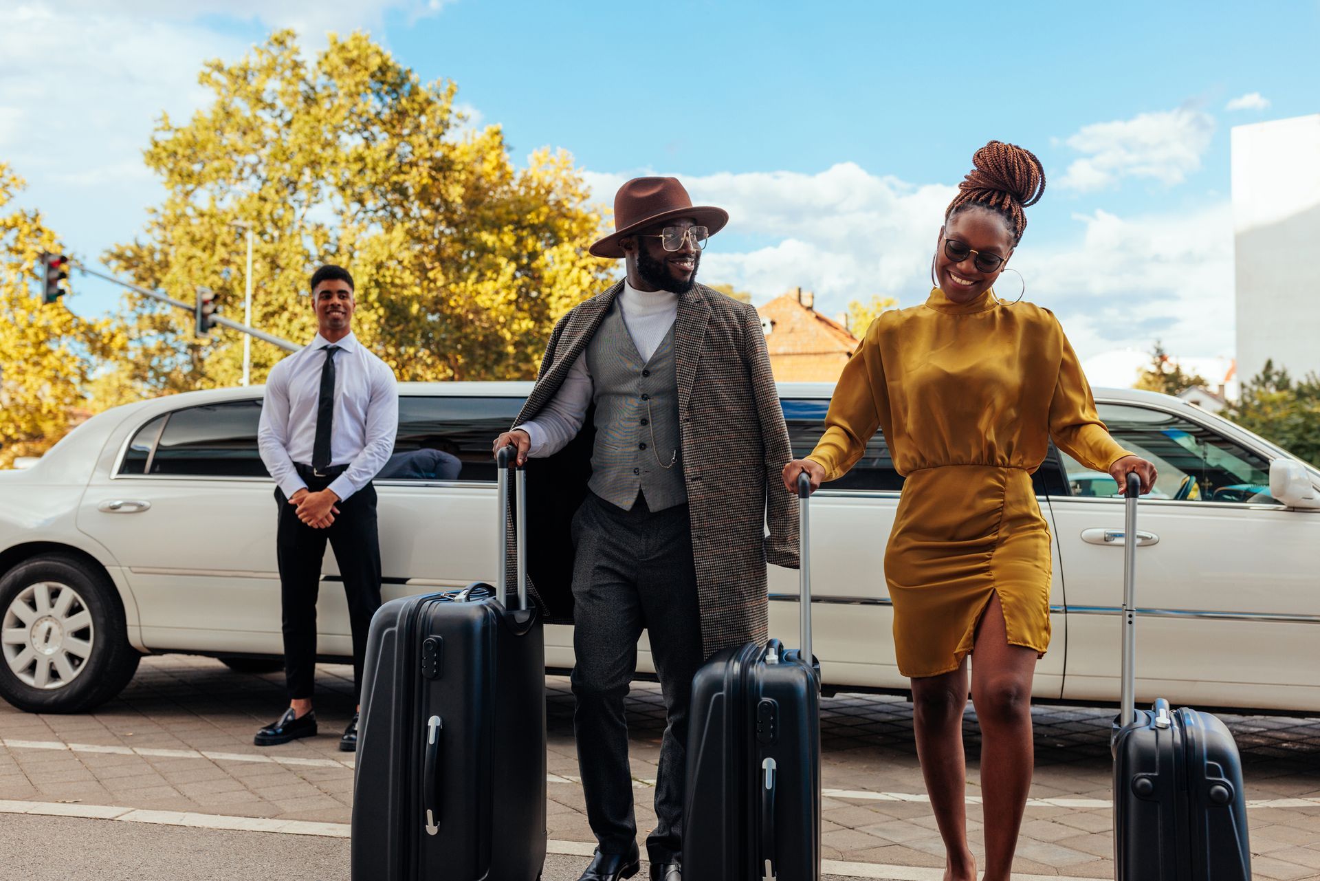 Driver standing beside a parked limousine as a couple arrives at their hotel from the airport.
