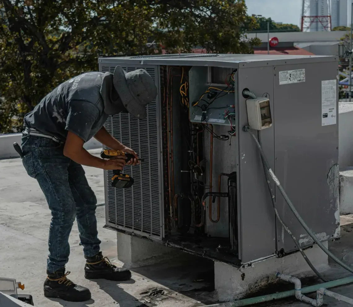 Technician repairing rooftop HVAC unit with tools on a sunny rooftop