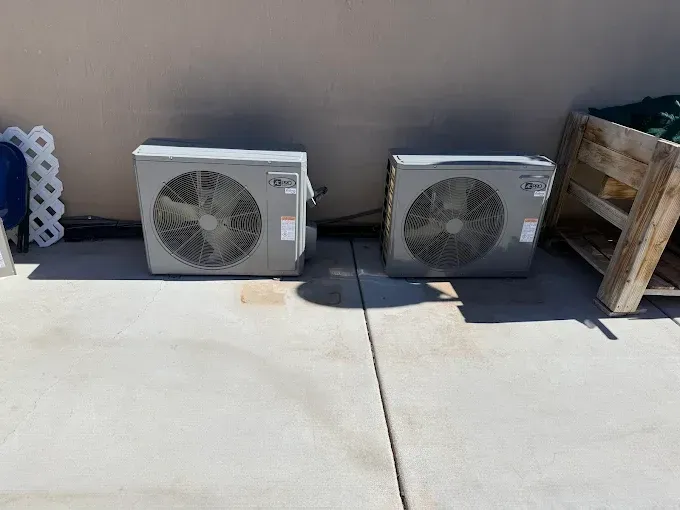 Two outdoor HVAC units on a concrete patio beside a wooden crate