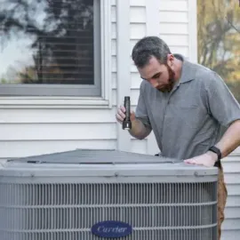 Technician inspecting an outdoor air conditioner beside a house window