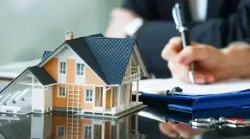 Miniature house model next to a person signing documents, possibly for a real estate transaction.