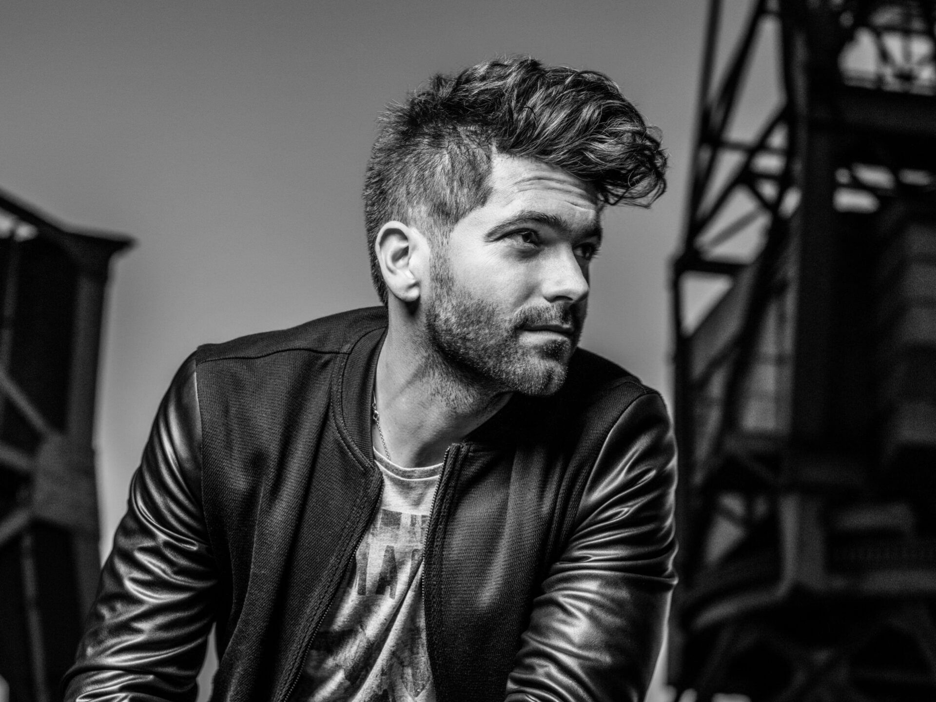 Man in black jacket looking off-camera with a neutral expression.