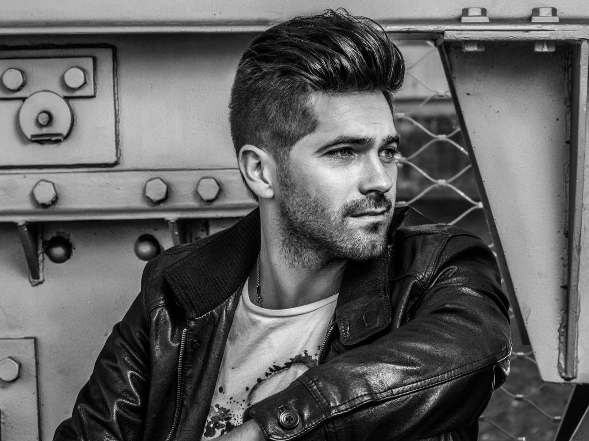 Man with pompadour hairstyle wearing a black leather jacket, looking off to the side with a serious expression.