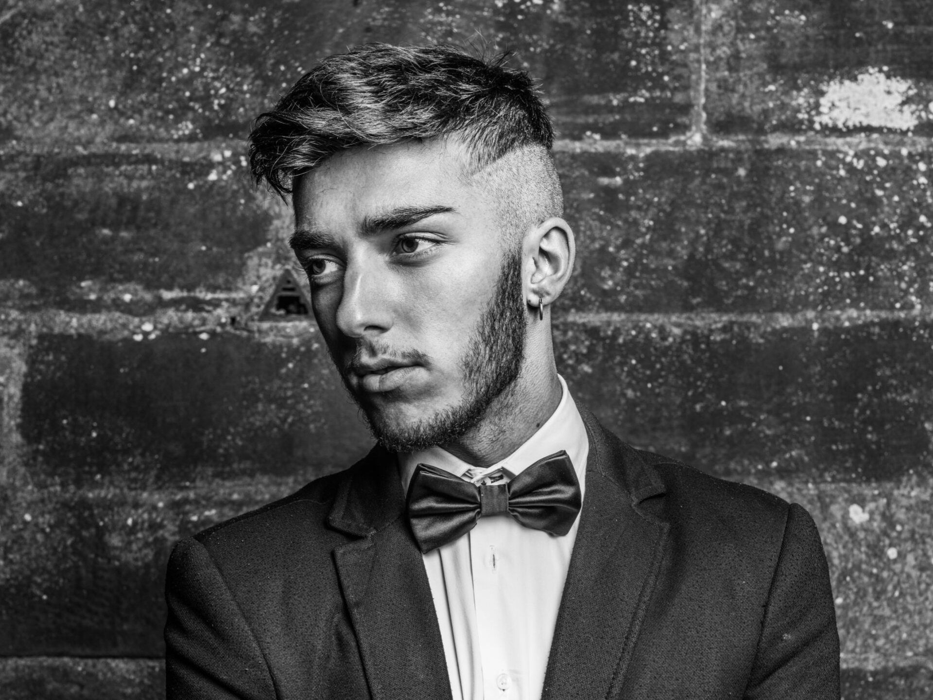 A man in a suit and bow tie is standing in front of a brick wall.