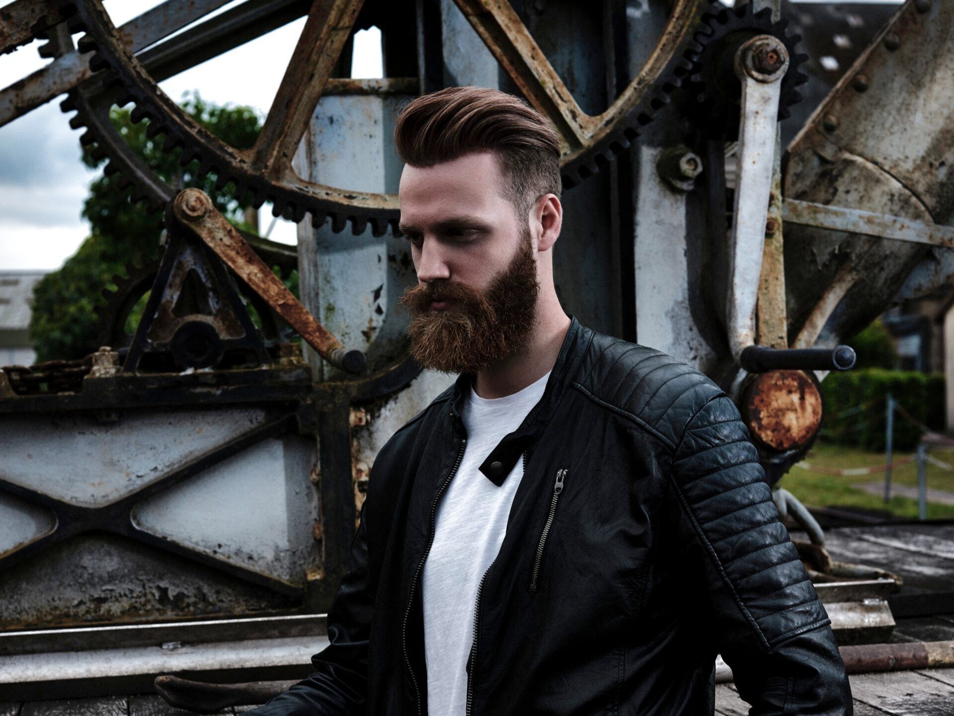 A man with a beard is wearing a black leather jacket and a white shirt.
