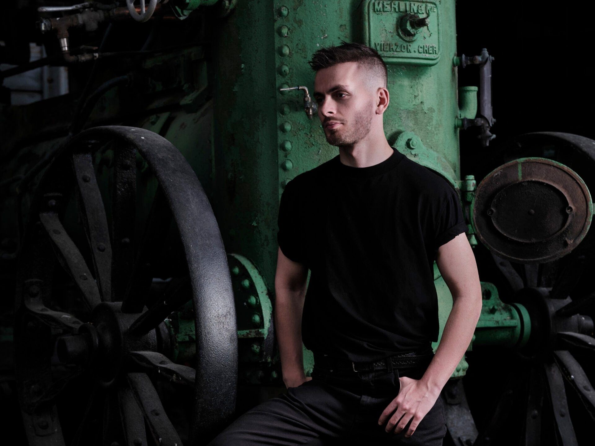 A man in a black shirt is sitting in front of a green machine.
