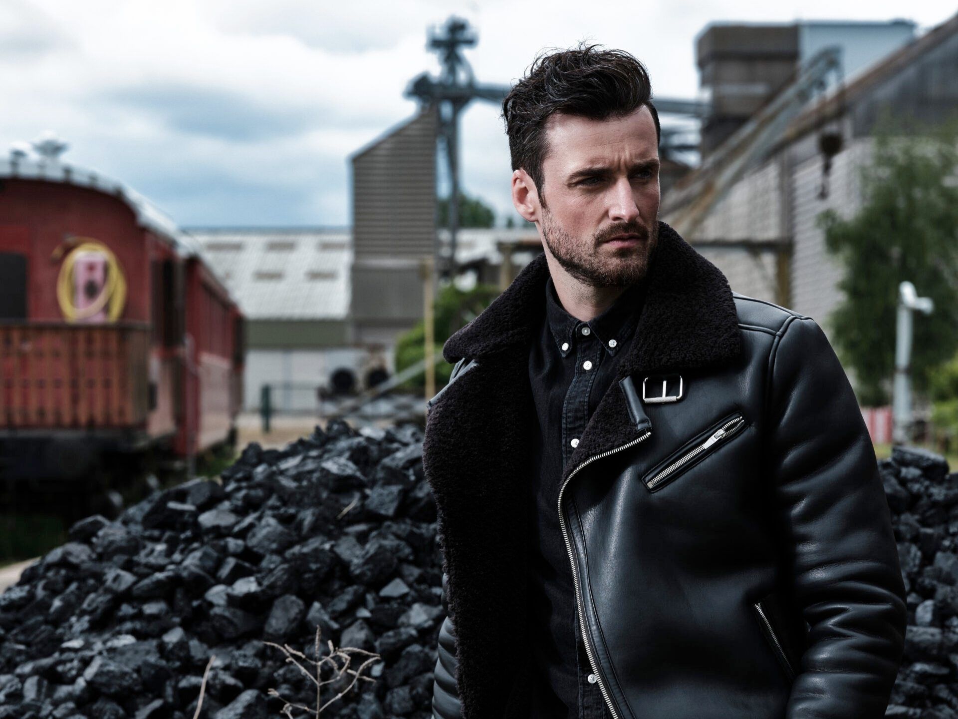 A man in a black leather jacket is standing in front of a pile of coal.