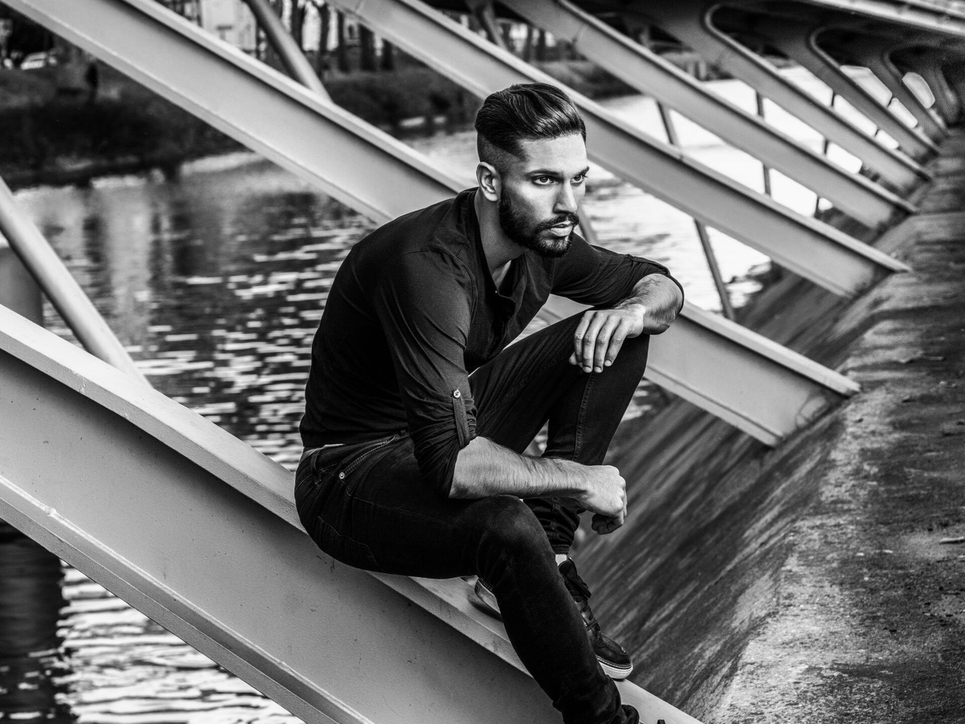 A black and white photo of a man sitting on a bridge.