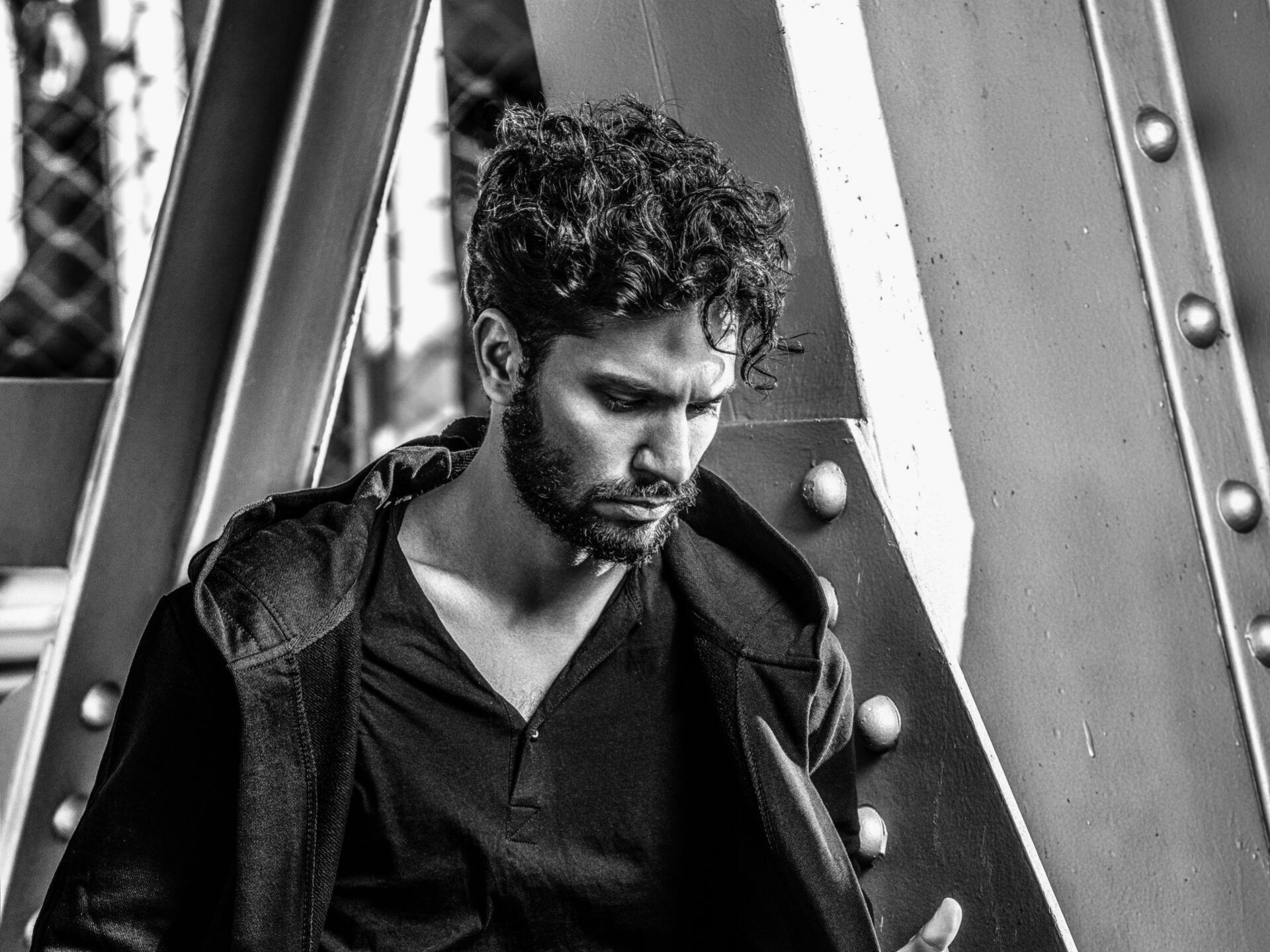 A black and white photo of a man standing under a bridge looking at his phone.