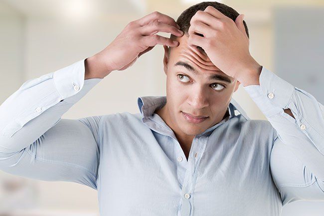 A man is looking at his hair in the mirror.