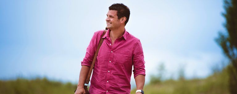 A man in a pink shirt is walking in a field.