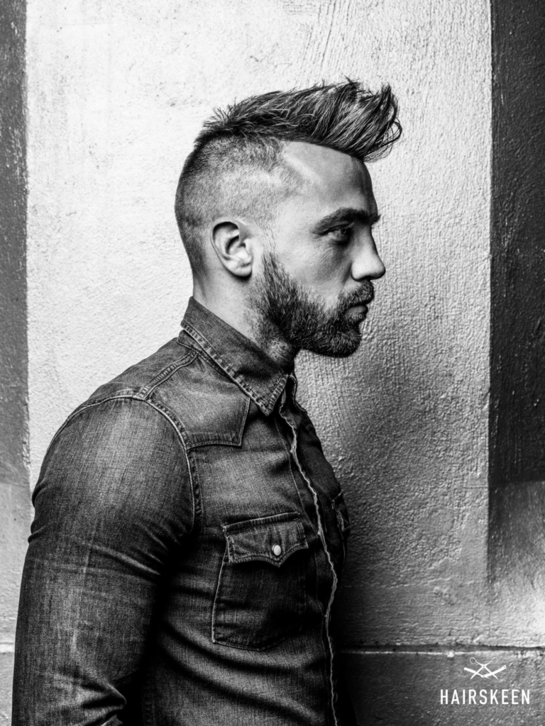 A black and white photo of a man with a mohawk and beard.