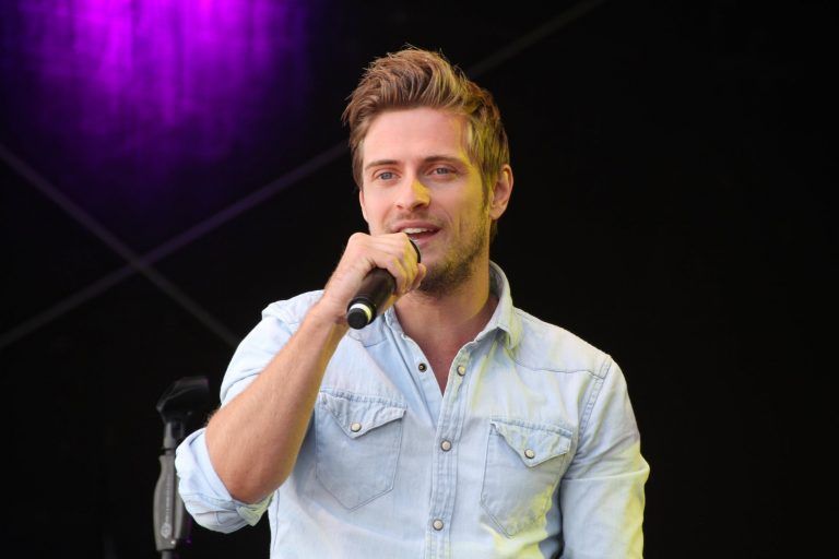 A man in a denim shirt is singing into a microphone.