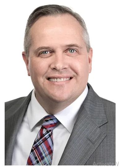 Man with gray hair, smiling, wearing a suit and tie.