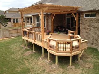 A wooden deck with a pergola attached to it in front of a brick house.