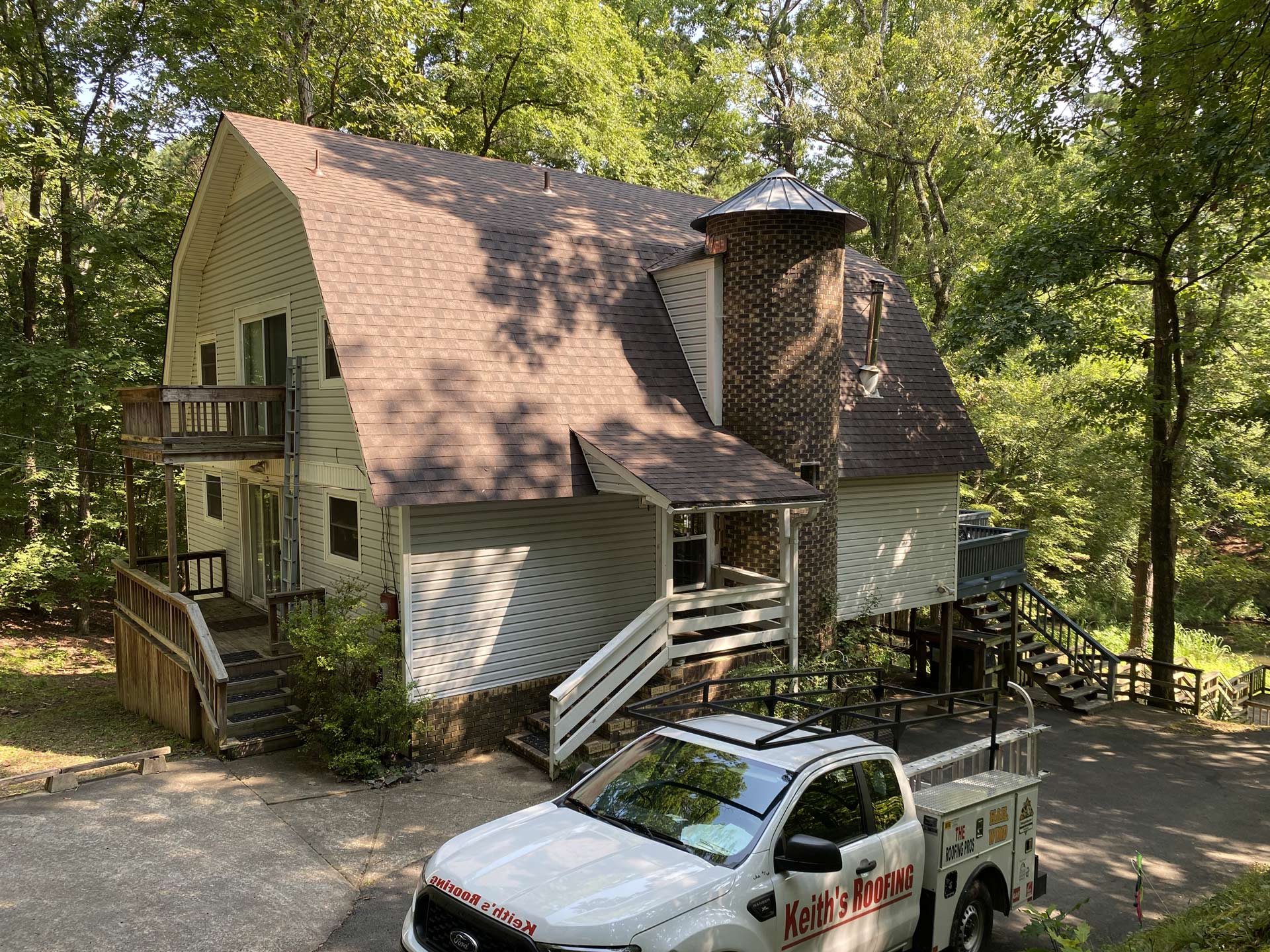 A white truck is parked in front of a house in the woods.