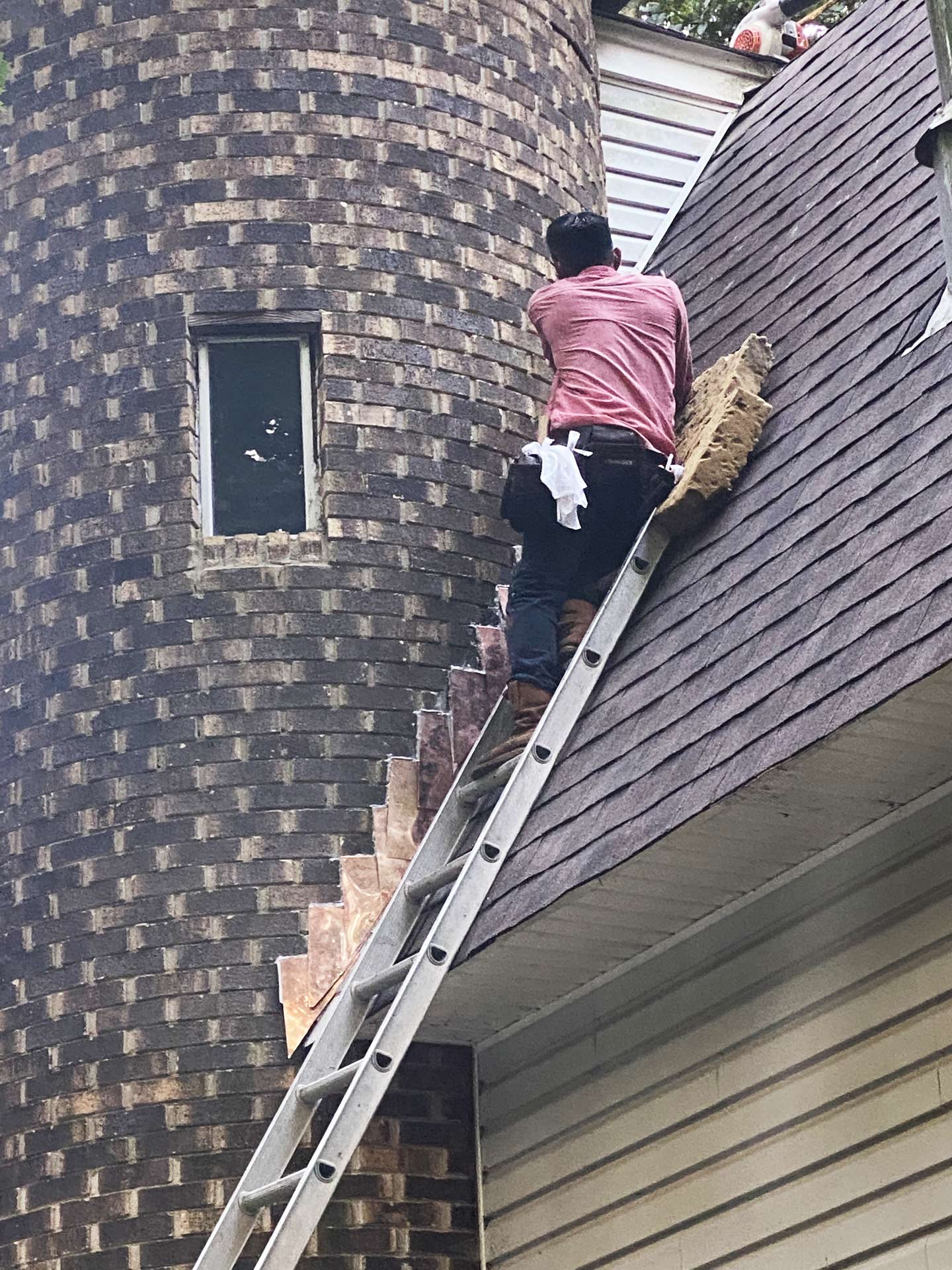 A man is sitting on a ladder on the roof of a house.