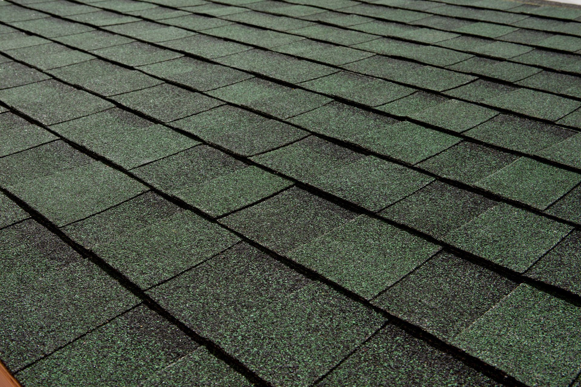 A close up of a roof with green shingles.