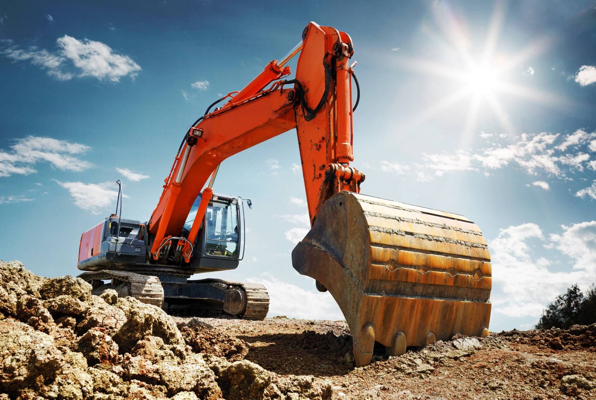 Orange excavator digging dirt at a construction site under a bright sunny sky