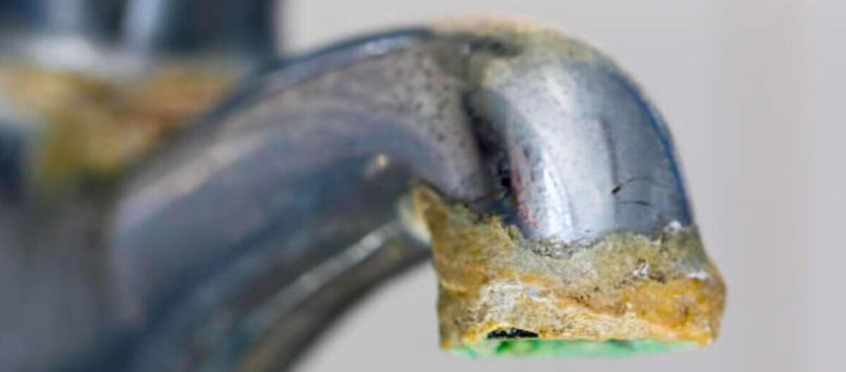 Close-up of white limescale deposits on a kitchen tap, showing mineral buildup caused by hard water.