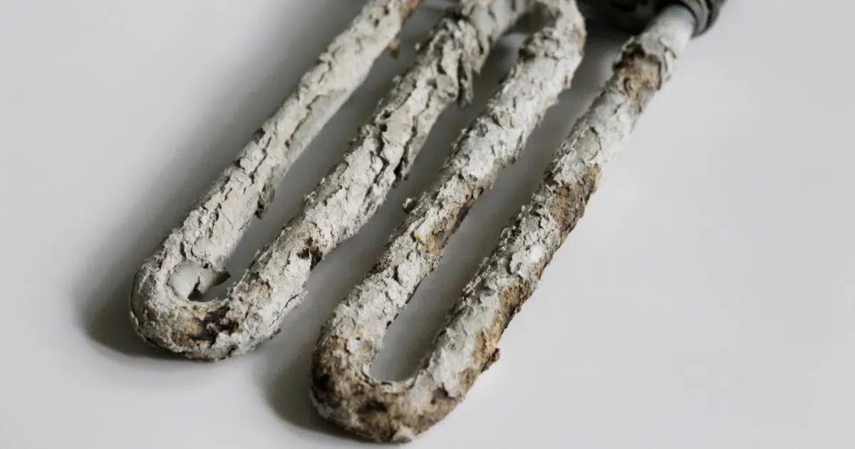 Close-up of an immersion heater element heavily coated with white limescale, showing mineral buildup