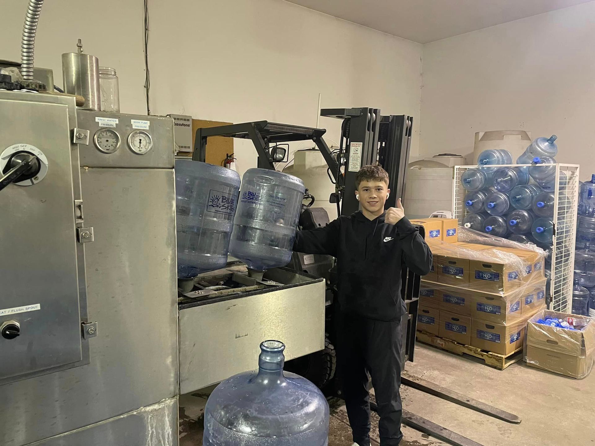 A man is standing next to a forklift in a room filled with water bottles.