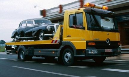 A yellow tow truck is carrying a black car