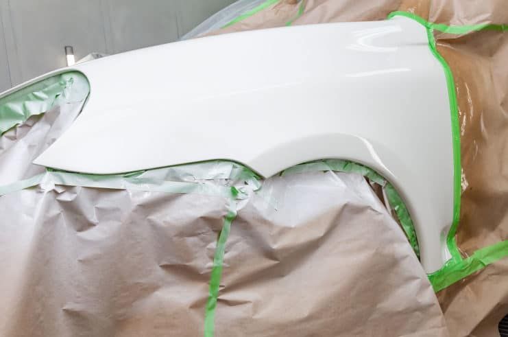 A white car fender is being painted with green tape.