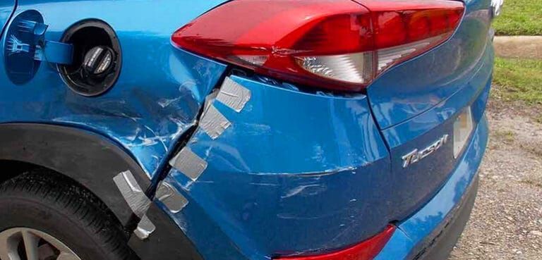 A blue car with a damaged bumper is parked on the side of the road.