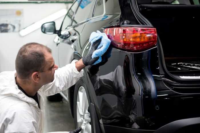 A man is polishing a black car with a blue cloth.