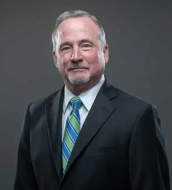 A man in a suit and tie is standing in front of a gray background.