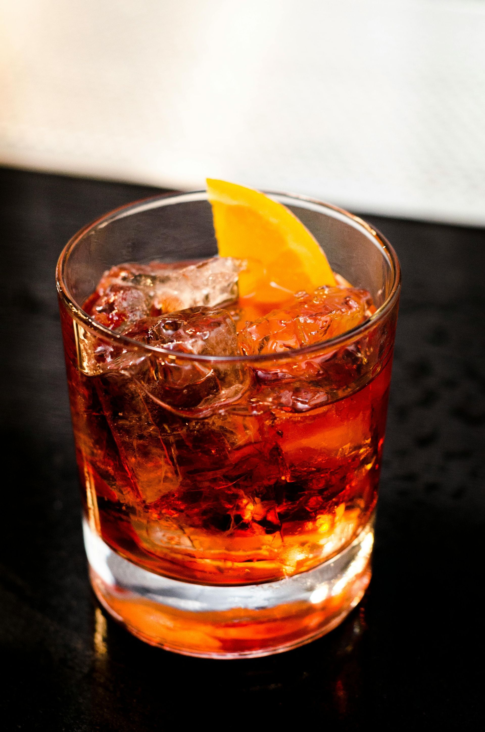 A close up of a glass of whiskey with ice and an orange slice on a table.