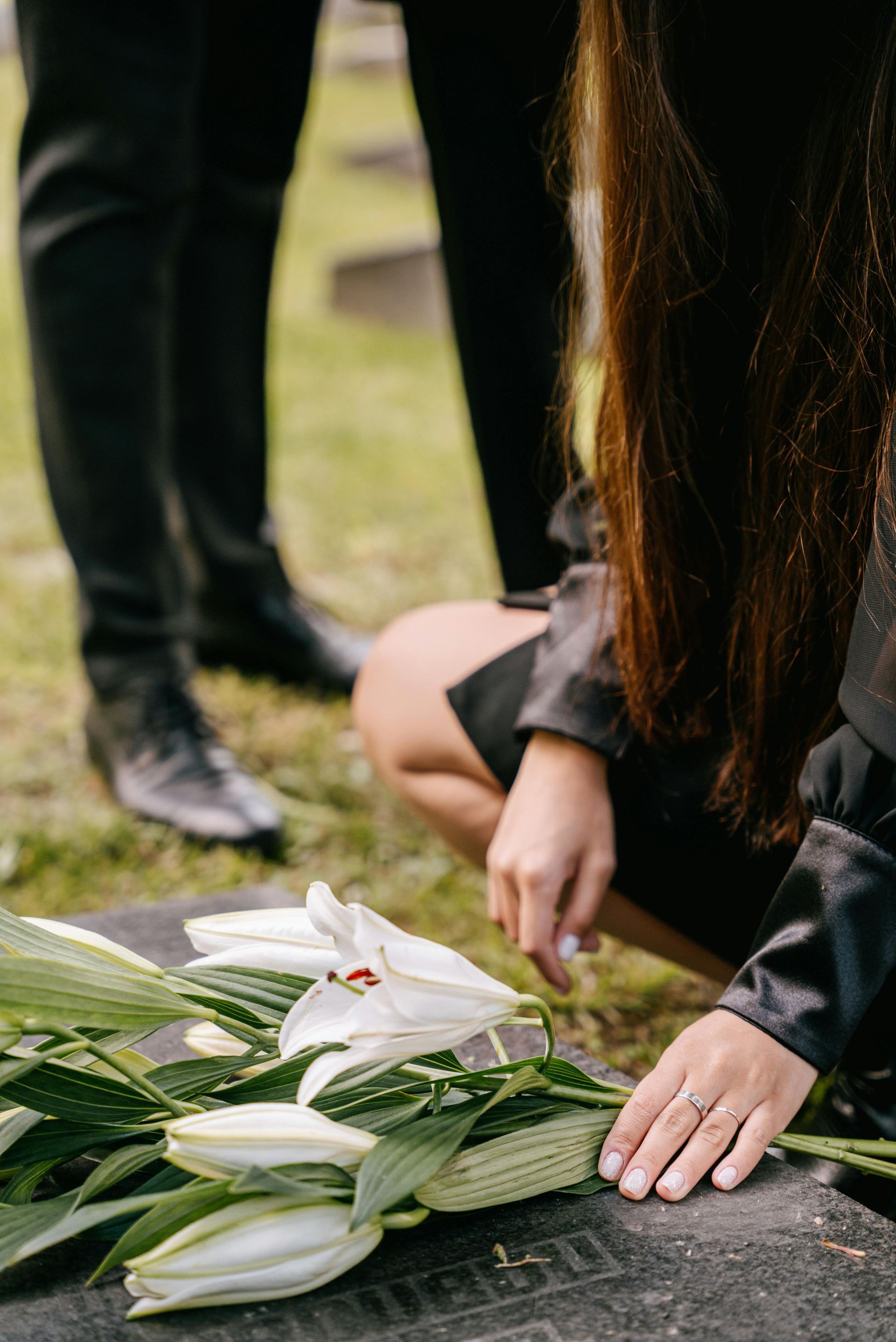 A woman is kneeling down to place flowers on a grave.